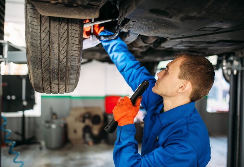 Mechanic with lamp checks the car suspension