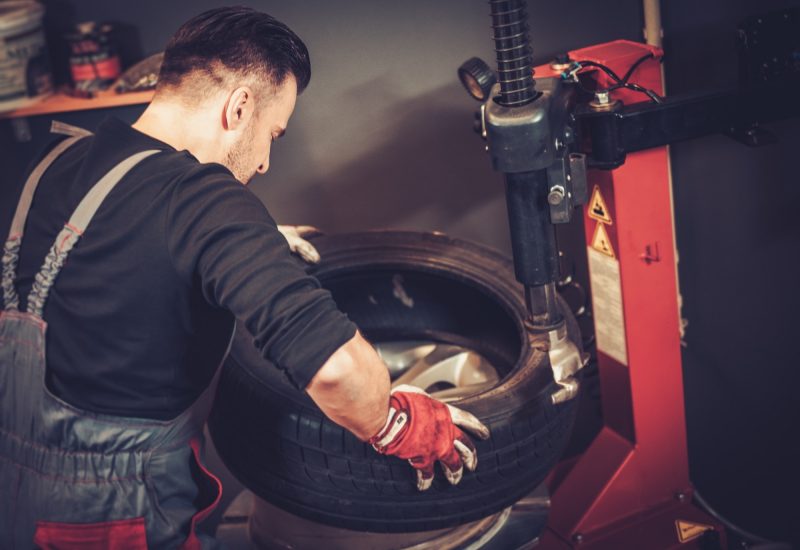 Professional car mechanic replace tire on wheel in auto repair service.